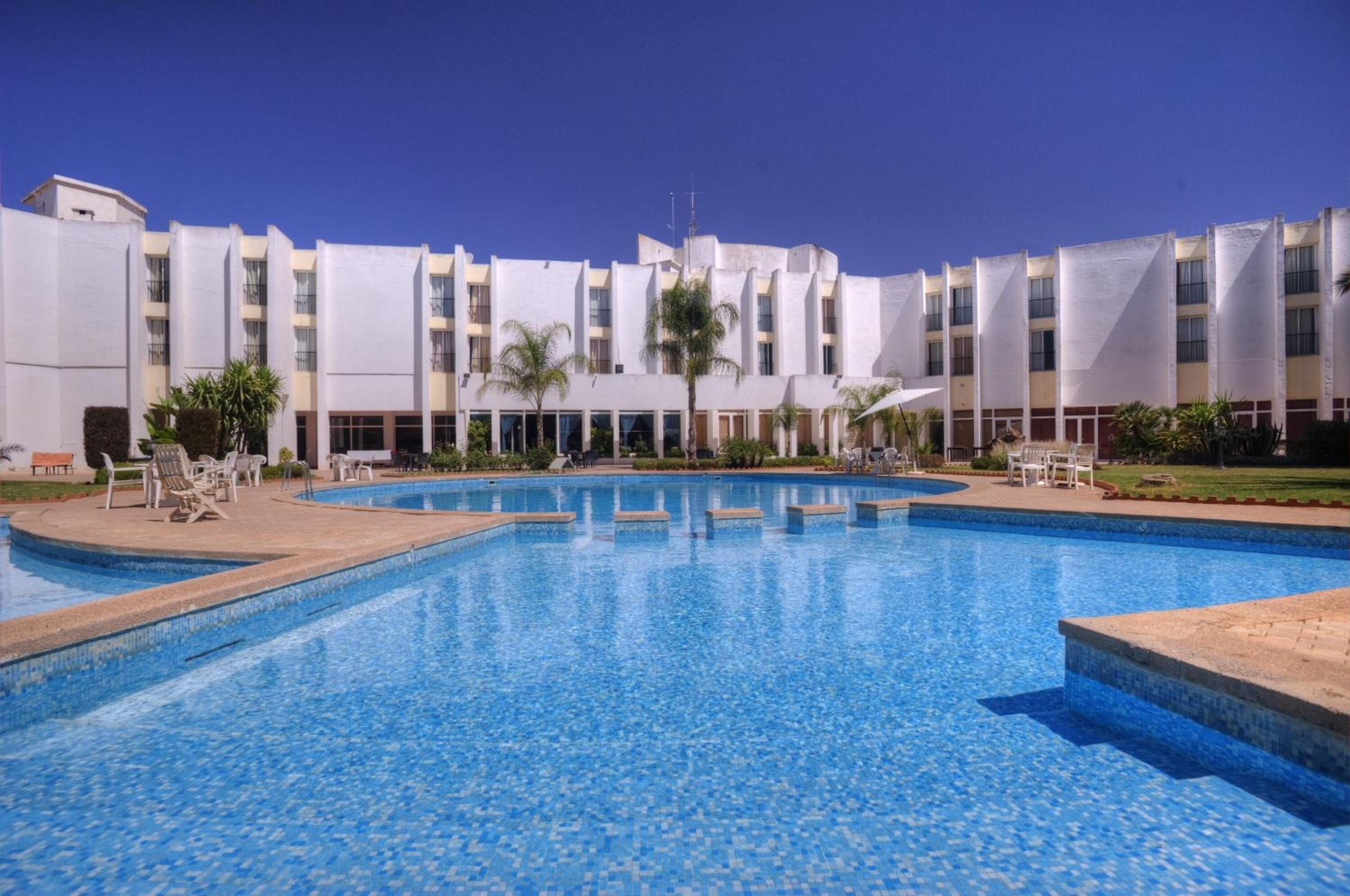 Una piscina con sillones de descanso y un edificio con varios balcones al fondo.