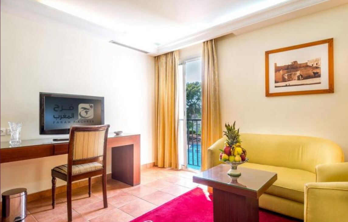 Une chambre d’hôtel équipée d’une télévision, d’un bureau, d’une chaise, d’un canapé et d’une fenêtre avec des rideaux.