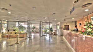 Un vestíbulo de hotel con mostrador de recepción, zona de estar y puertas de vidrio que dan al exterior.