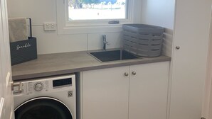 A compact kitchen with a washing machine, a sink, and a window with a view of the outside. - Skibo Cottage (Skibo)