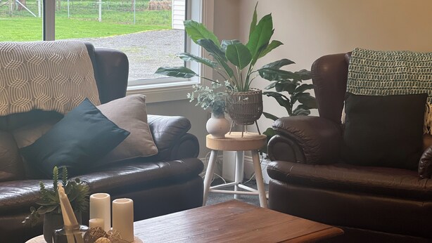 A living room with a brown leather sofa, a patterned throw, a small side table with a plant, and a window overlooking a grassy area. - Skibo Cottage (Skibo)