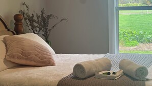 A bed with a white quilt, a wooden headboard, and a vase with dried plants. - Skibo Cottage (Skibo)