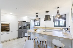 A modern kitchen with a central island, stainless steel appliances, pendant lighting, and a large window.
