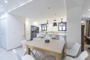 Una cocina moderna con armarios blancos, una mesa de comedor con sillas e iluminación colgante.