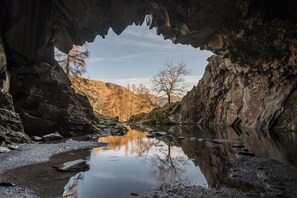 Entrada natural a una cueva con un río tranquilo que refleja el paisaje circundante.