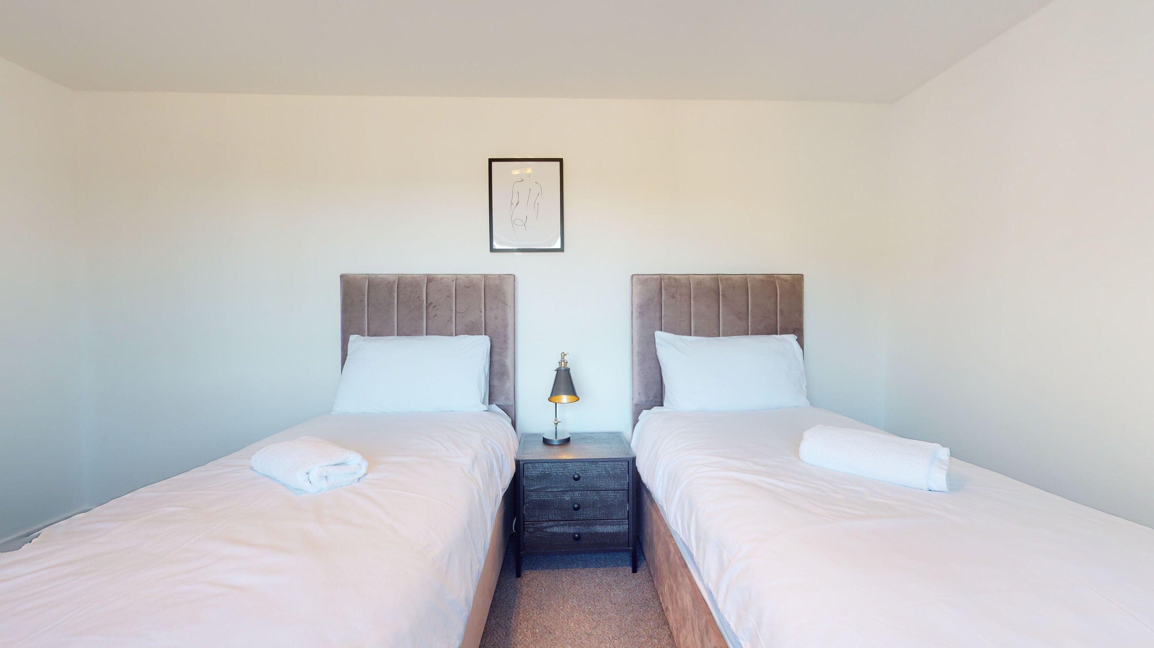 A twin room with two beds, a nightstand, a lamp, and a framed picture on the wall.