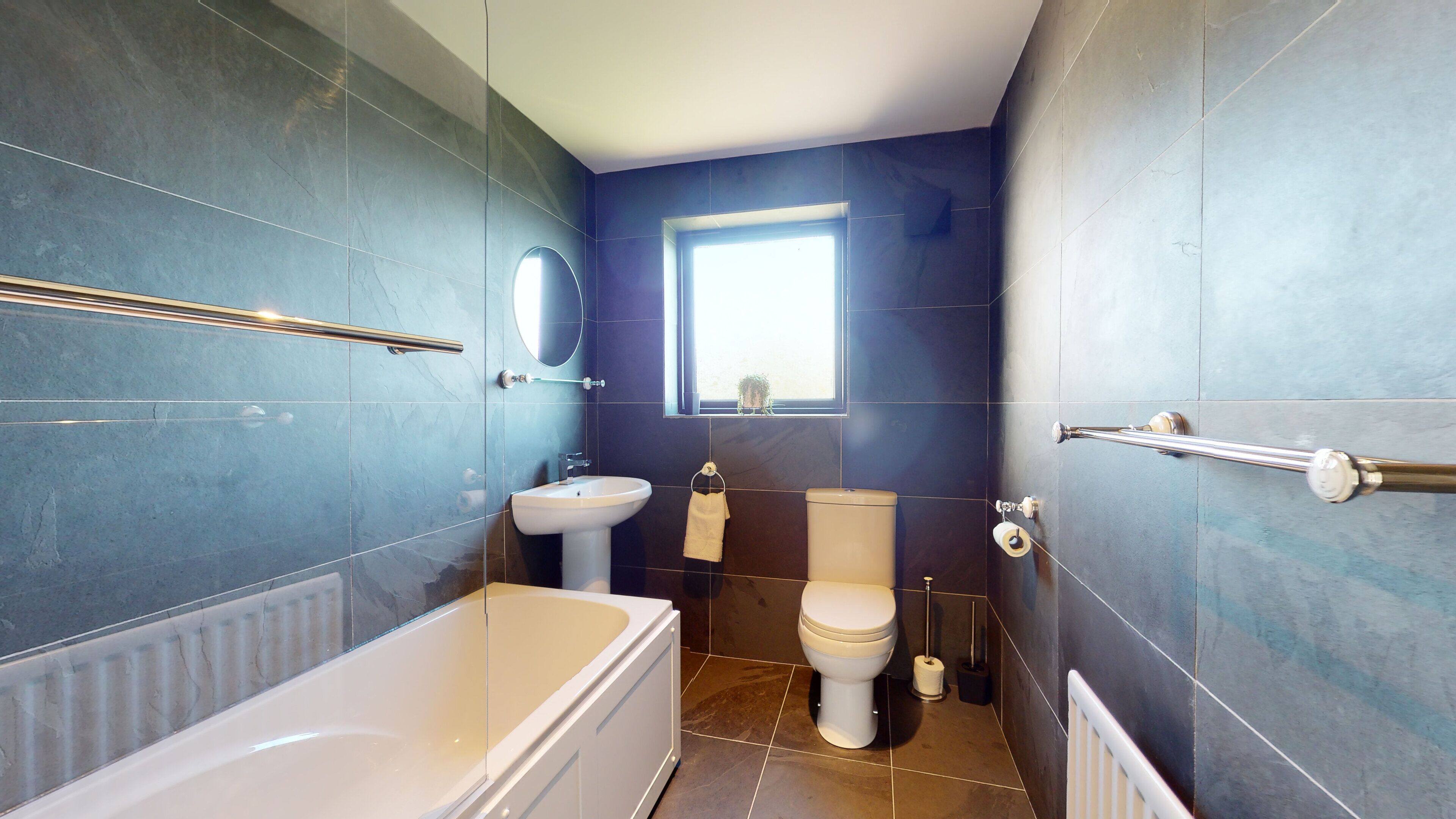 A modern bathroom with a bathtub, sink, toilet, and a window providing natural light.