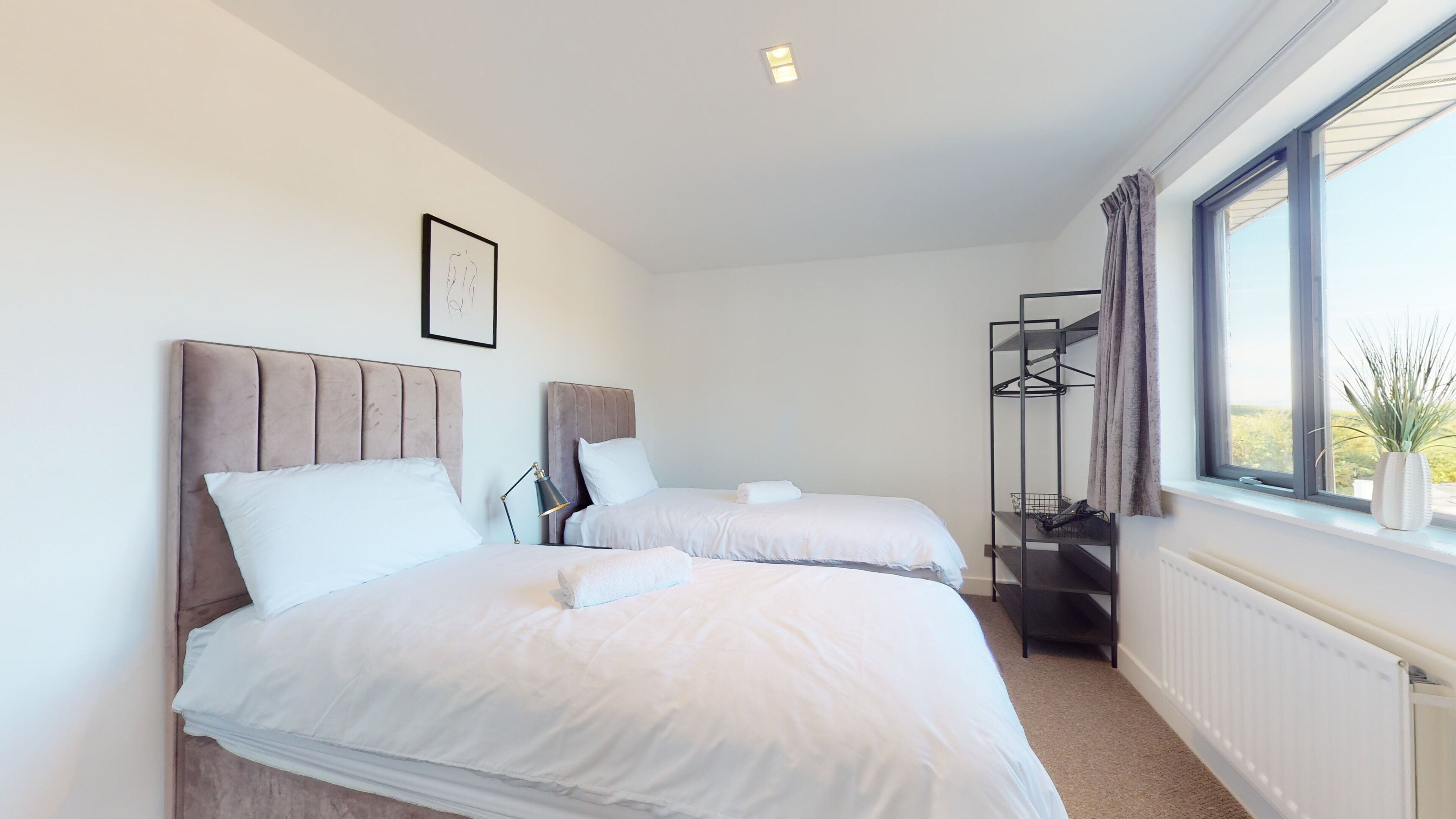 Een moderne hotelkamer met twee bedden, een radiator, een raam met uitzicht en een wandplank met een plant.