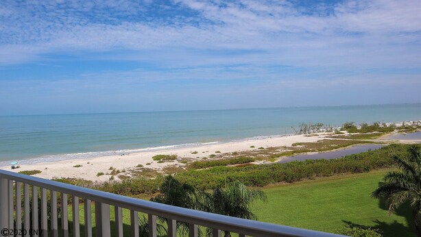 Blick auf einen Strand vom Balkon mit Geländer, klarer Himmel und ruhiges Meer.