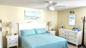 Ein Schlafzimmer mit einem Bett, Nachttischen, einer Kommode, einem Deckenventilator und einem Bild an der Wand.