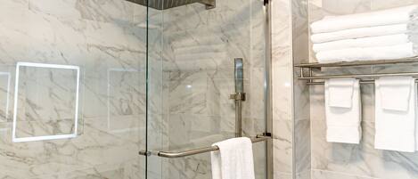 A modern bathroom with a glass-enclosed shower, a white bathtub, and a towel rack with neatly folded towels.