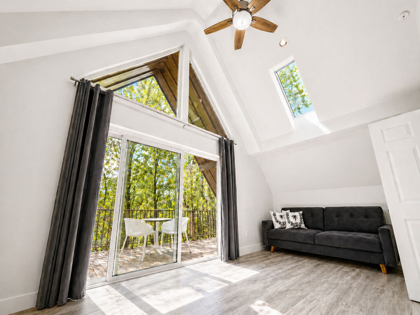 Amplia habitación con un gran ventanal corredero que da a un espacio exterior, ventilador de techo y sofá de color oscuro.