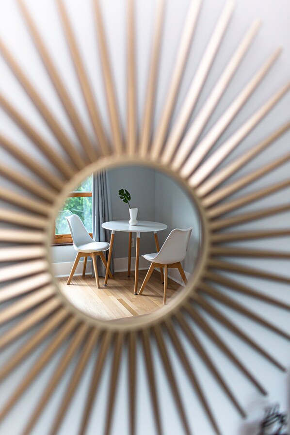 Una habitación con un espejo redondo que refleja un comedor, una ventana con cortinas y una planta sobre la mesa.