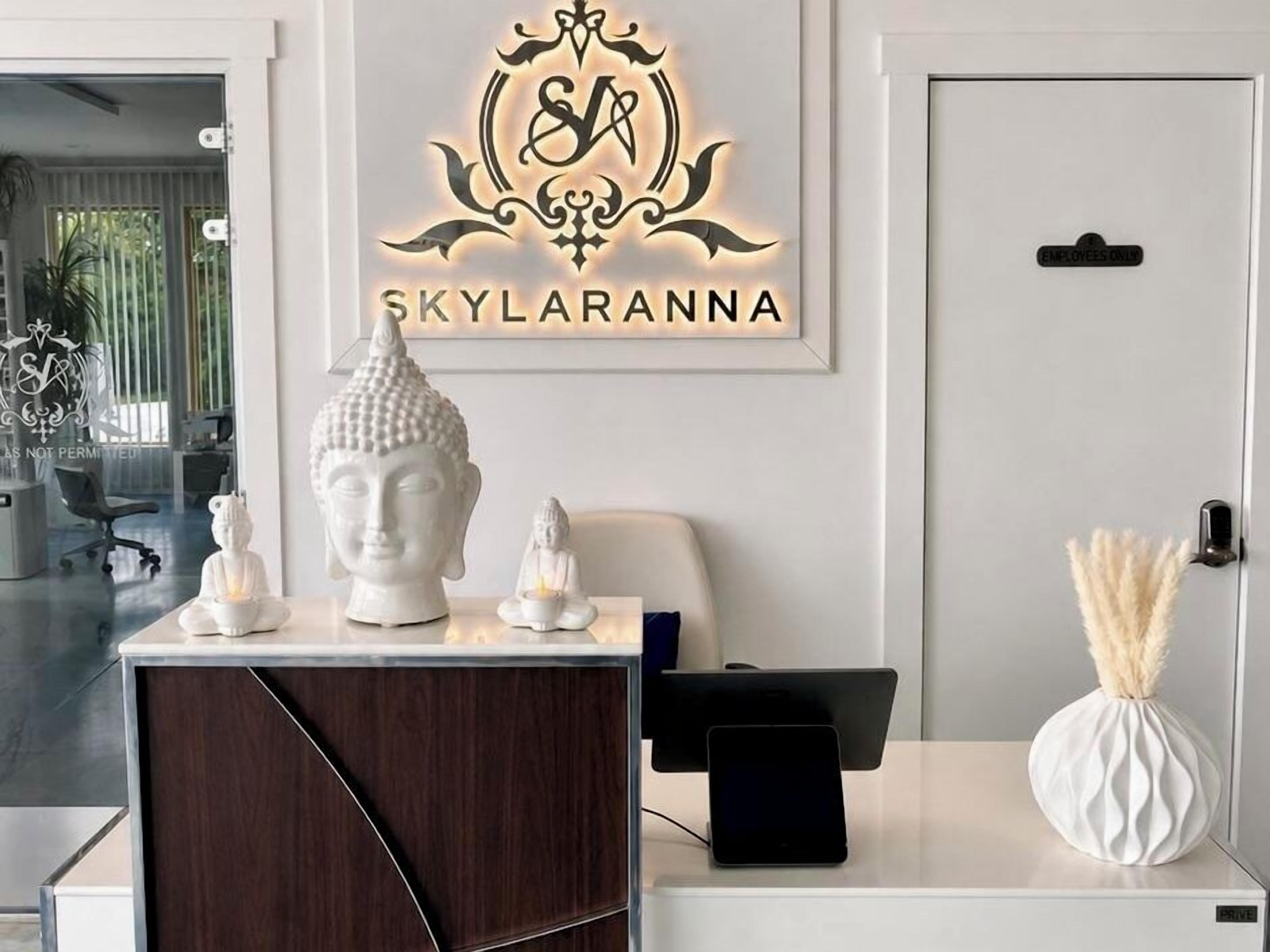 Un mostrador de recepción con un logotipo en la parte superior, un busto blanco y un jarrón con plumas de pampa.