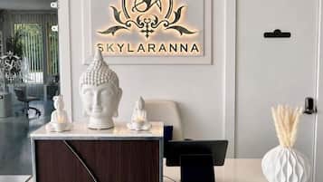 Un mostrador de recepción con un logotipo en la parte superior, un busto blanco y un jarrón con plumas de pampa.