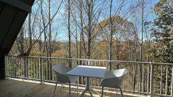 A wooden deck with a table and chairs, surrounded by a white railing, overlooking a forested area.