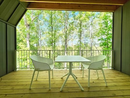 A wooden deck with a table and two chairs, overlooking a forested area.