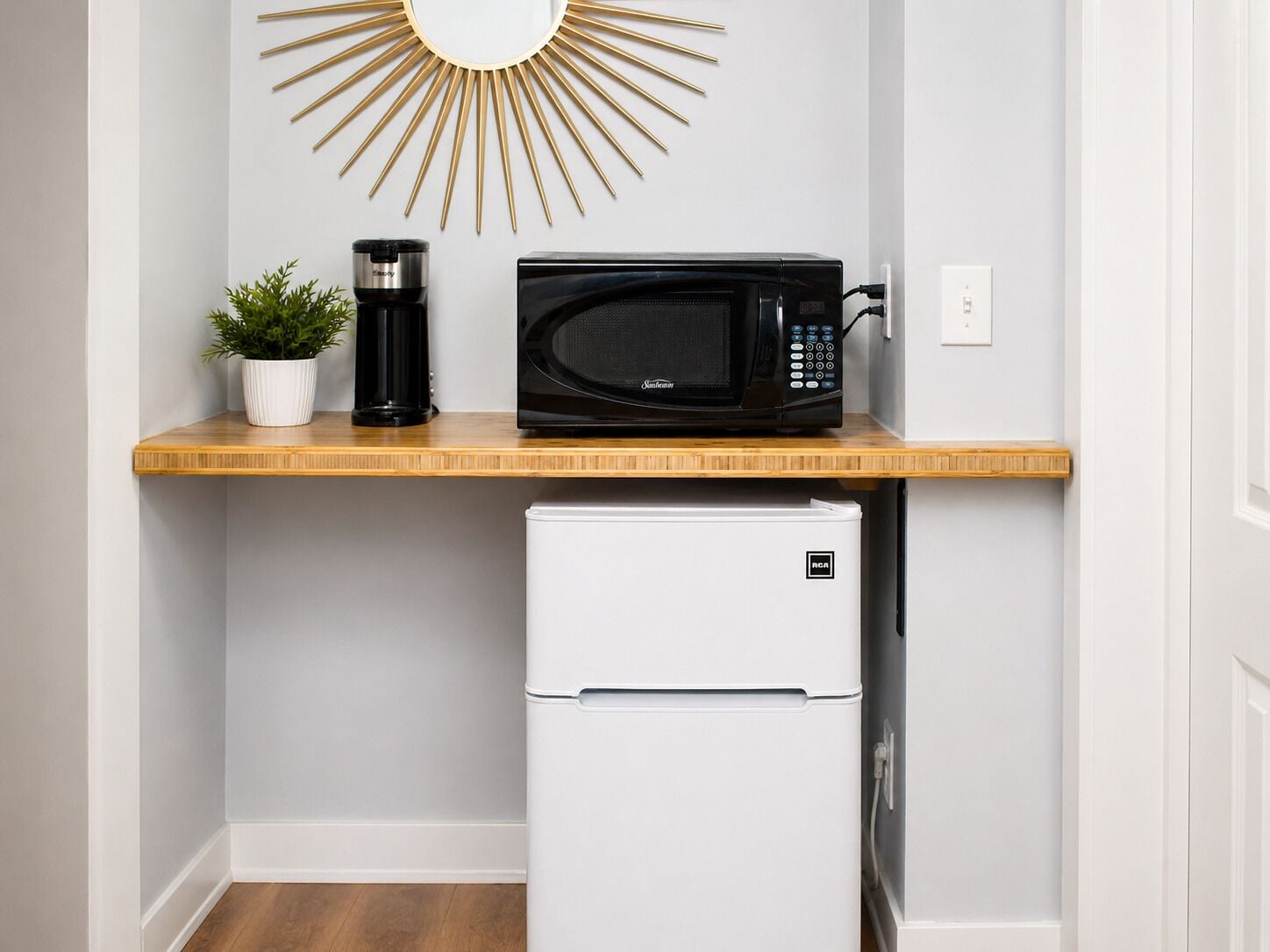 Una kitchenette compacta con microondas, cafetera y un refrigerador pequeño.