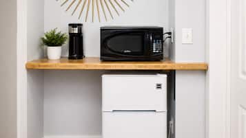 Una kitchenette compacta con microondas, cafetera y un refrigerador pequeño.