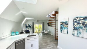 Una cocina moderna con una isla central, una zona de comedor con mesa y sillas, y una escalera que sube a un nivel superior.