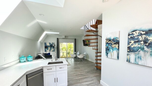 Una cocina moderna con una isla central, una zona de comedor con mesa y sillas, y una escalera que sube a un nivel superior.
