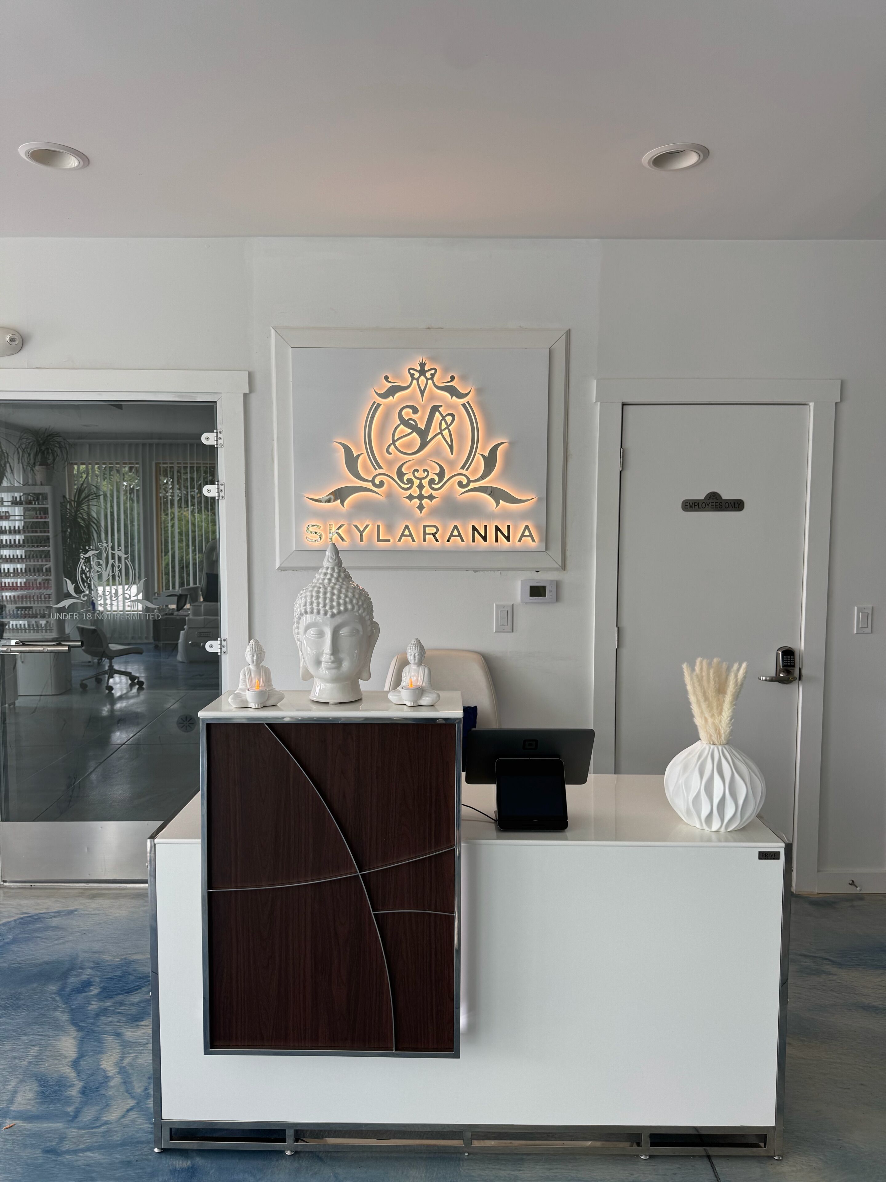 A reception desk with a logo, a Buddha statue, a vase, and a door labeled 'EMPLOYEES ONLY'.