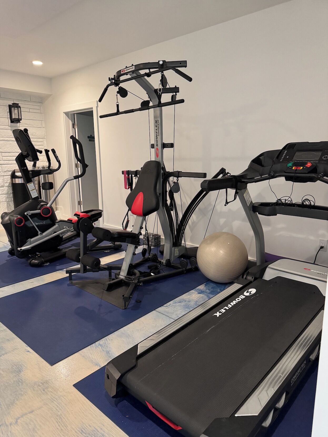 A home gym with a treadmill, elliptical, and weight machine.