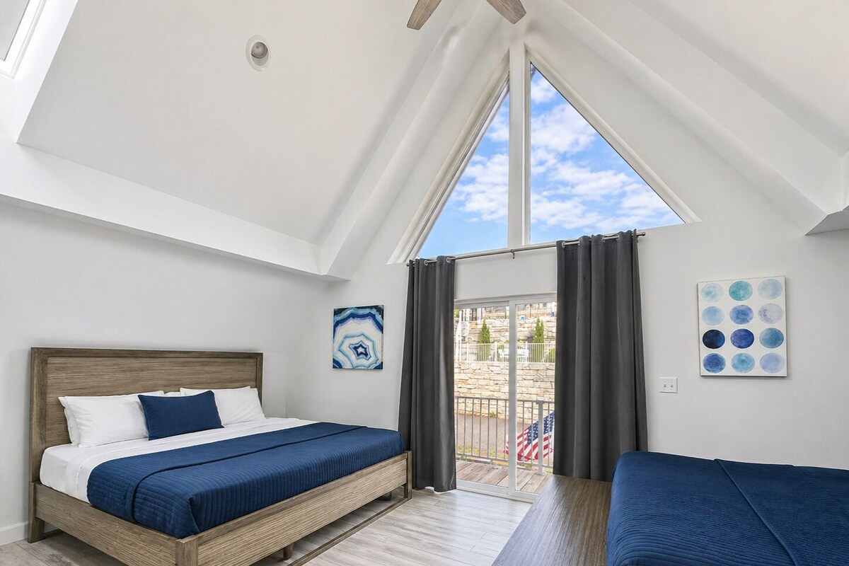 Un dormitorio con cama, una mesita de noche, vistas a través de una ventana y un techo con tragaluces.