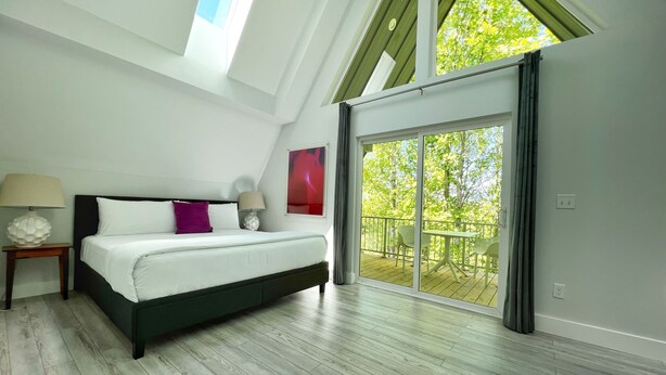 Un dormitorio con cama, mesita de noche, lámpara y vistas a un balcón con mobiliario exterior.