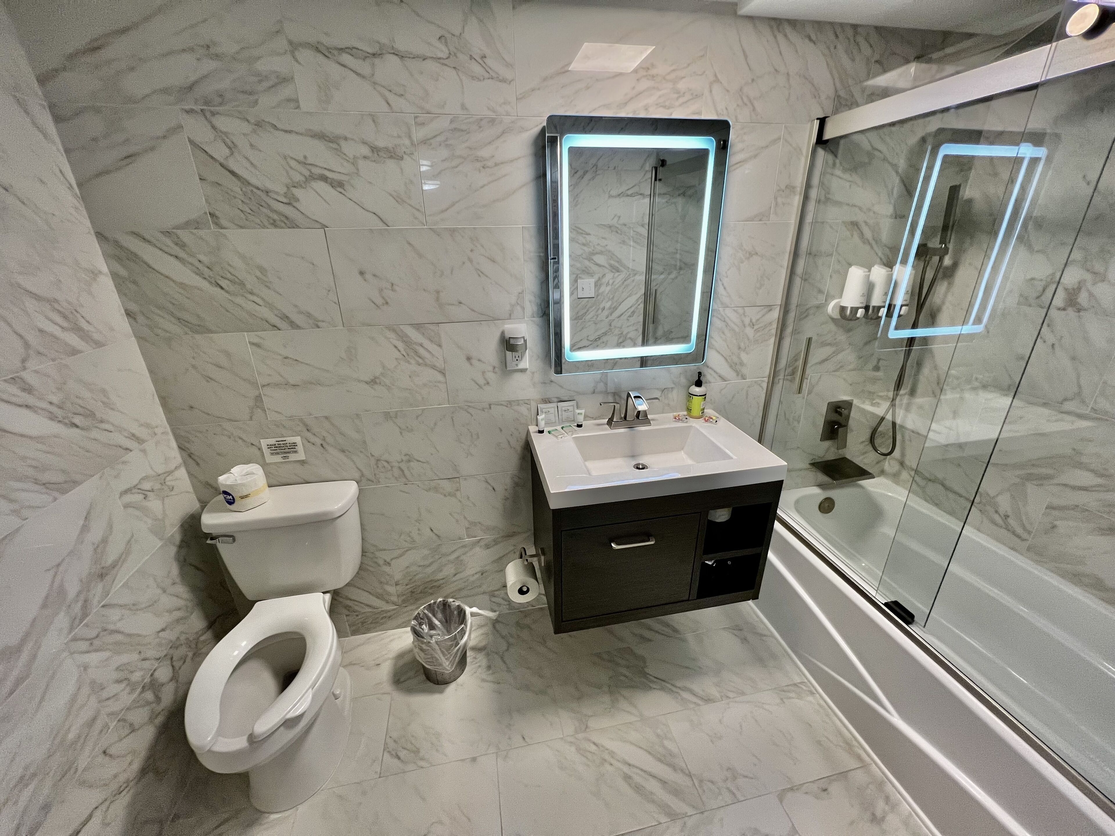 A modern bathroom with a marble floor, a white toilet, a sink with a mirror, and a glass shower enclosure.