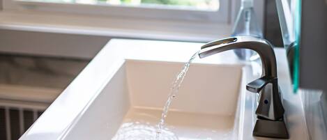 A bathroom sink with running water, a window, and a view of greenery outside.