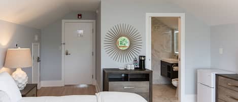 Habitación de hotel con cama, mesita de noche, lámpara, decoración en la pared y una zona de kitchenette.