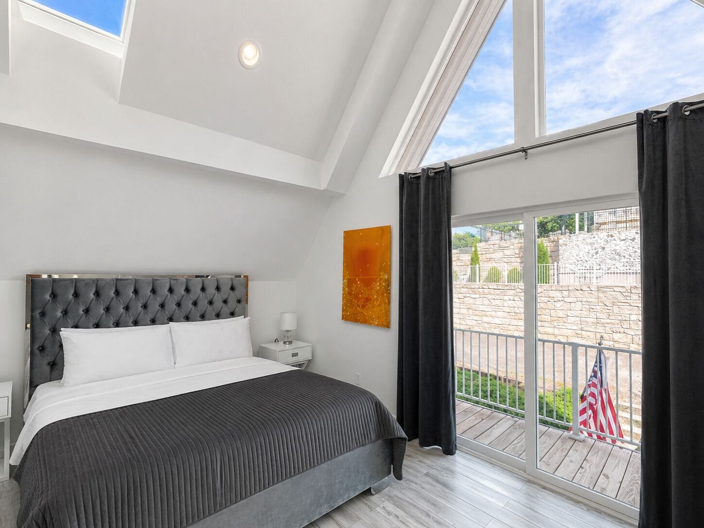 Un dormitorio con cama, mesita de noche, ventana con cortinas y vistas al exterior.