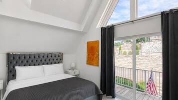 Un dormitorio con cama, mesita de noche, ventana con cortinas y vistas al exterior.