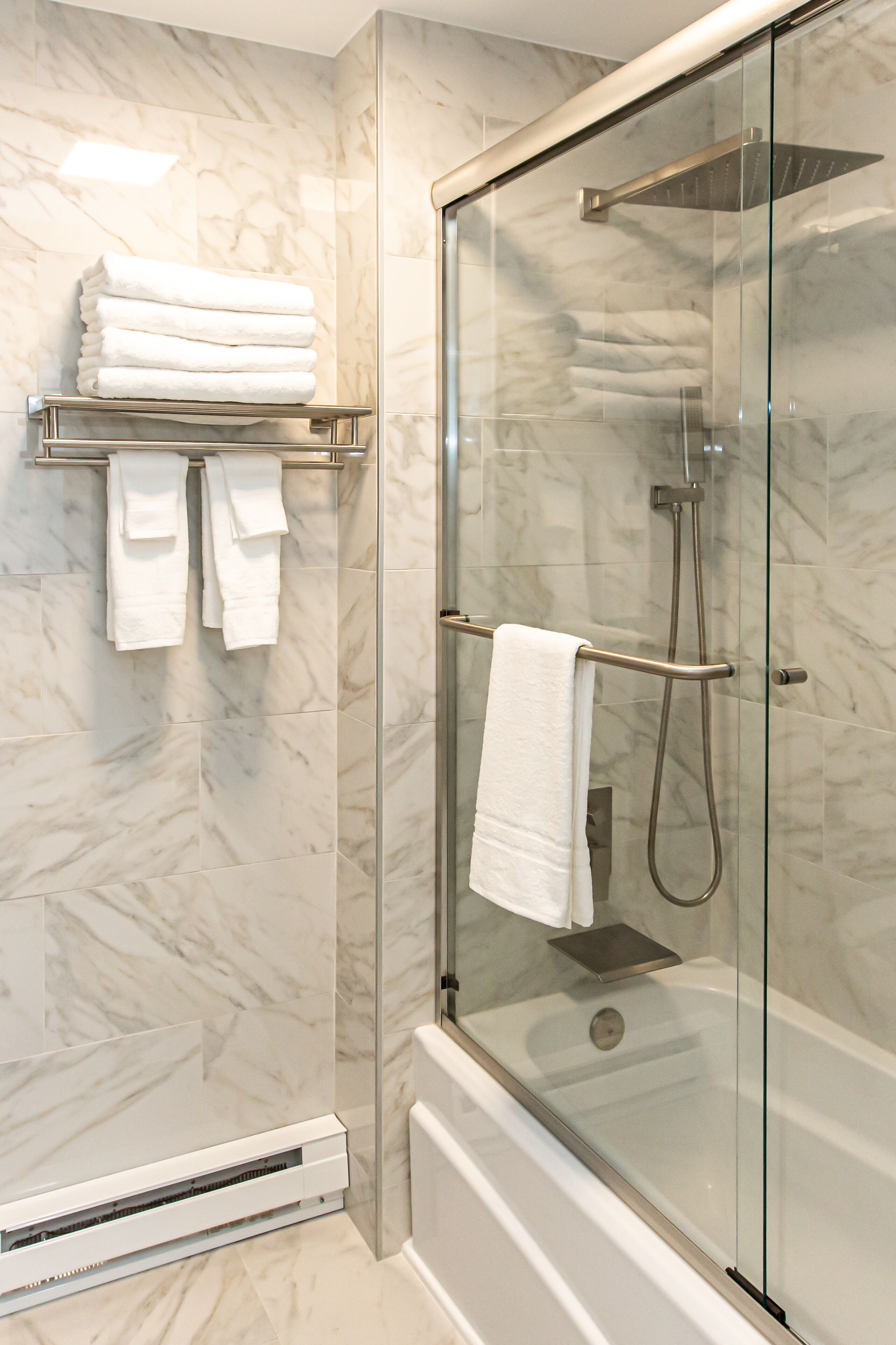 Ein modernes Badezimmer mit einer gläsernen Duschkabine, Marmorwänden und ordentlich drapierten Handtüchern.