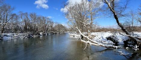 A river with snow-covered banks and trees, under a clear blue sky.