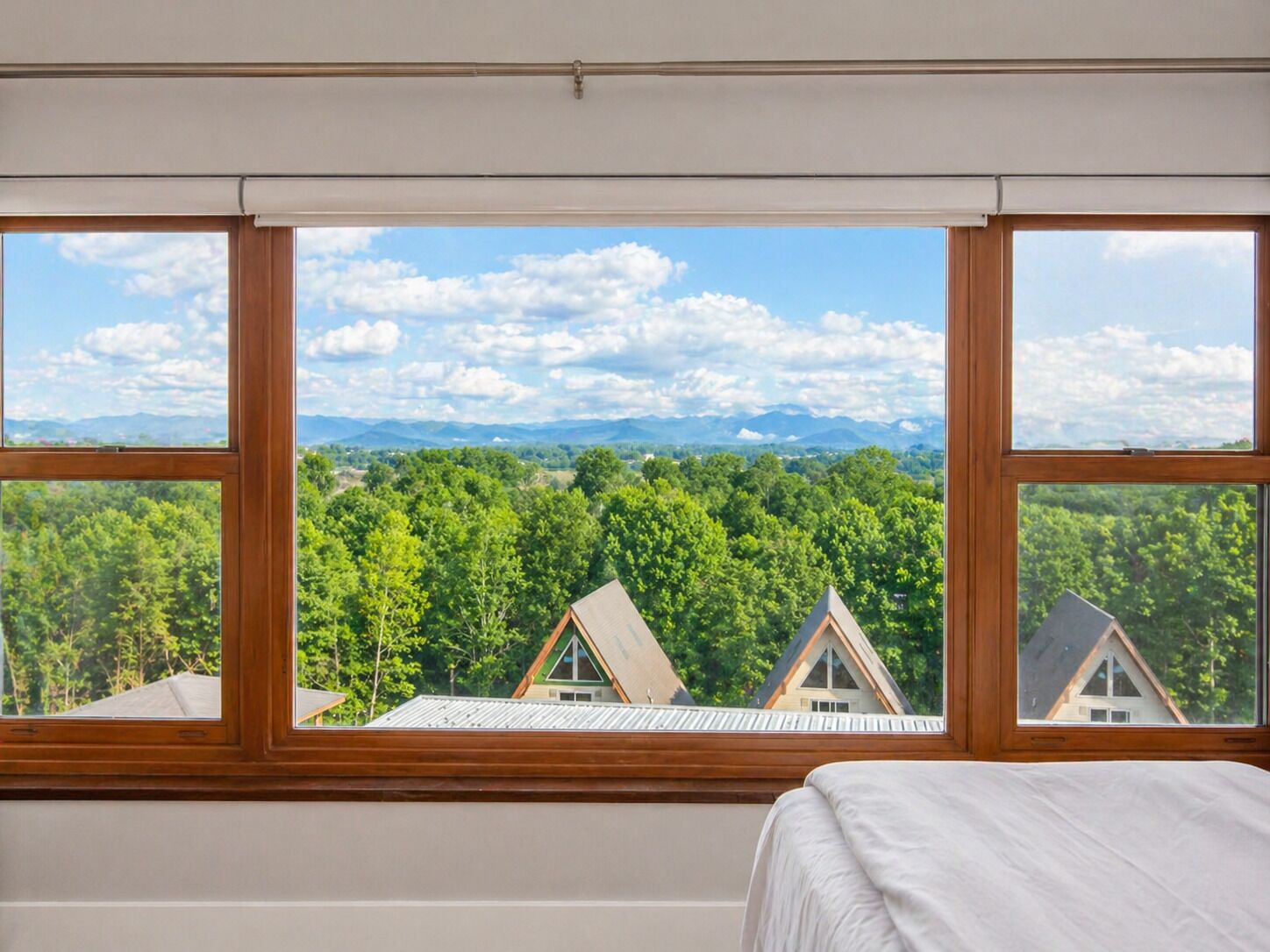 Una habitación con un amplio ventanal que da a un área boscosa y montañas distantes.