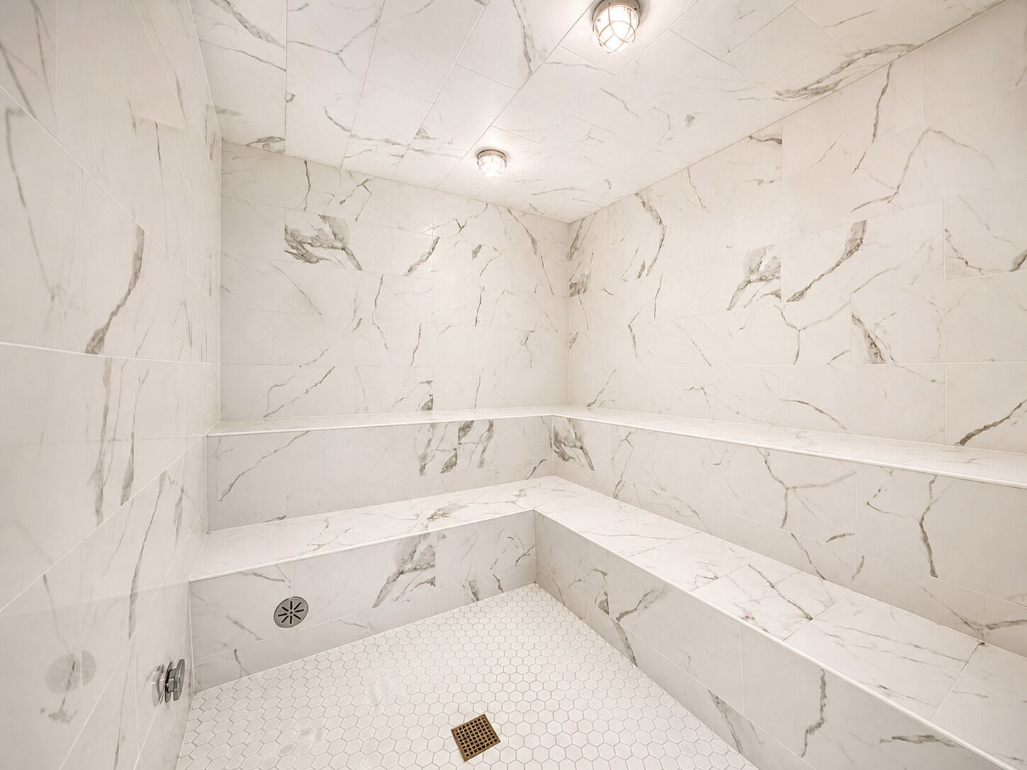 A bathroom with marble walls and floors, a shower with a hexagonal tile pattern, and a built-in shelf.