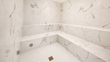 A bathroom with marble walls and floors, a shower with a hexagonal tile pattern, and a built-in shelf.