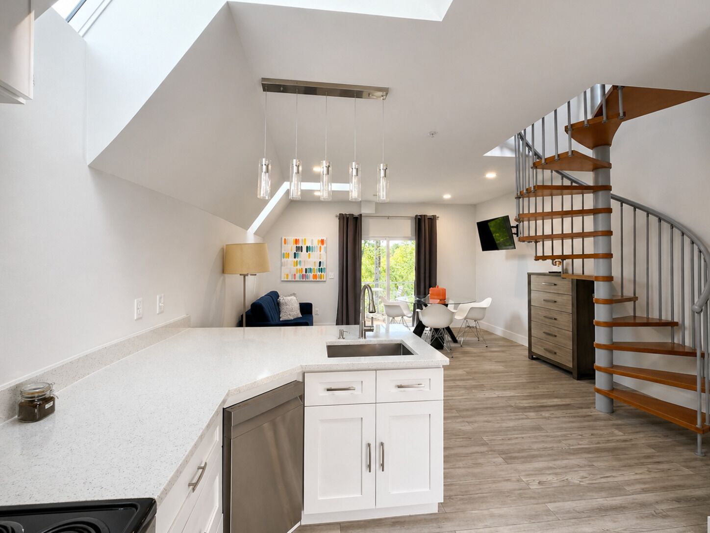 A modern kitchen with a central island, a dining area with a table and chairs, and a staircase with wooden steps.