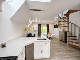A modern kitchen with a central island, a dining area with a table and chairs, and a staircase with wooden steps.