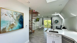 Una cocina moderna con armarios blancos, un lavamanos de acero inoxidable y una escalera de madera que conduce a un balcón.