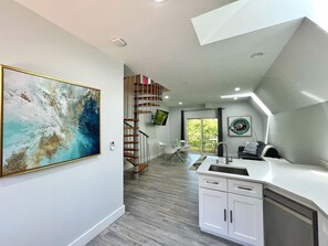 Una cocina moderna con armarios blancos, un lavamanos de acero inoxidable y una escalera de madera que conduce a un balcón.