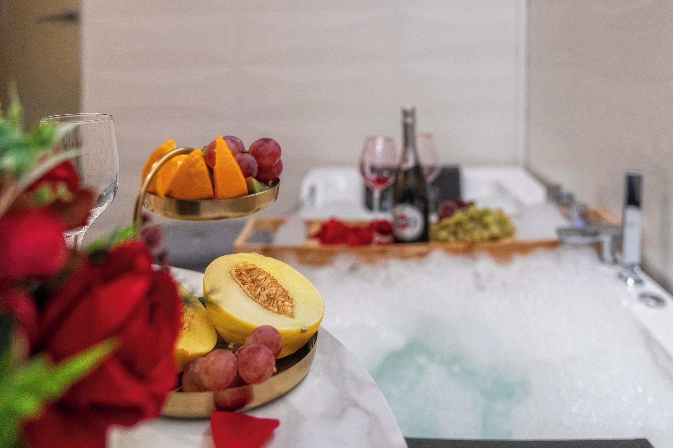 A bathroom with a bathtub, a bowl of fruit, and a wine bottle.