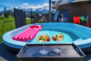 A poolside setting with two cocktails on a tray, a pink inflatable float, and a view of mountains in the background. - Górski Resort Zakopane (Poronin)