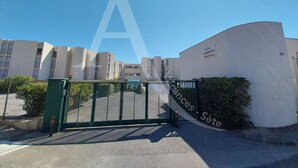 A gated entrance to a residential building complex with multiple apartment buildings in the background. - REZ DE CHAUSSEE, 1ERE LIGNE MER, ACCES DIRECT PLAGES (Sète)