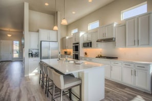 A spacious kitchen with white cabinets, a large island with bar stools, and a view of the outdoors through the windows.