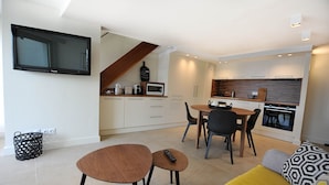 A modern kitchen with white cabinets, a microwave, and a stove. There is a dining area with a table and chairs, and a TV mounted on the wall. - Apartment facing the beach (Cannes)