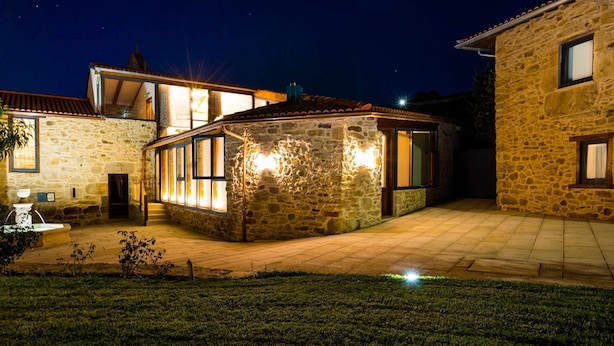 Un bâtiment en pierre avec un toit en tuiles, une entrée bien éclairée et un petit jardin.