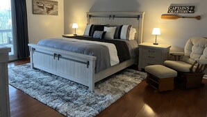 Un dormitorio con cama, mesitas de noche, una silla, ventilador de techo y un letrero en la pared.